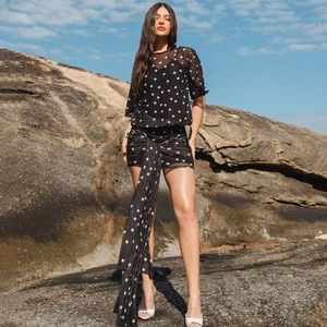 Detail of black polka dot sheer top and ruffled mini skirt with long ties on a female model
