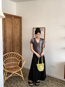 Detail showing a yellow woven bucket bag paired with a dark brown tie-dye V-neck shirt