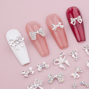 Détails de bijoux à ongles nœuds argentés avec perles et strass sur un fond rose doux