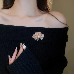 Close-up of pink enamel flower brooch with a center pearl on a black knitted sweater