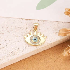 Detail shot of a gold Evil Eye pendant with blue zircon on a textured stone surface