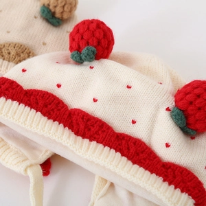 Gedetailleerde gebreide textuur van de gebroken witte babymuts met aardbeienpatroon