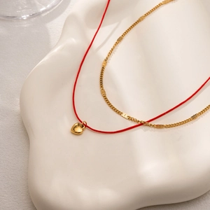 Détail du cordon rouge et du pendentif cœur en acier doré 18K sur collier double rang