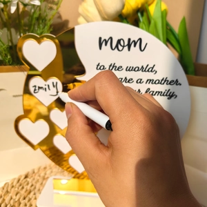 Close-up of hand writing a name on a customized heart-shaped Mother's Day acrylic ornament