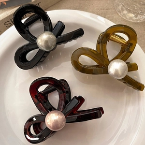 Detailed view of pearl-embellished hair claws in black, amber, and tortoiseshell on a tray