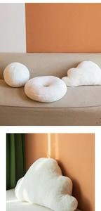 Three white plush decorative pillows in ball, donut, and cloud shapes on a cozy sofa