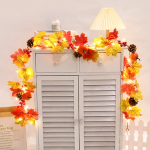 Detail of warm LED maple leaf garland with mini pumpkins and pinecones on white cabinet