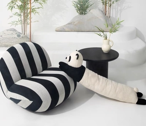 Détail d'un long oreiller en peluche panda sur un canapé rayé avec décor minimaliste de bambou