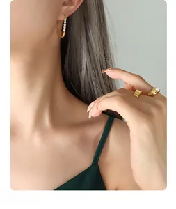 Detailed shot of gold paperclip earrings with pearls and matching rings on model