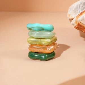 Gros plan de cinq bagues irrégulières en acrylique empilées aux tons vert et ambre