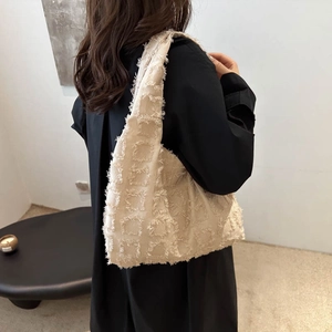 Stylish cream-colored fringe tote bag worn on shoulder in a minimalist urban setting
