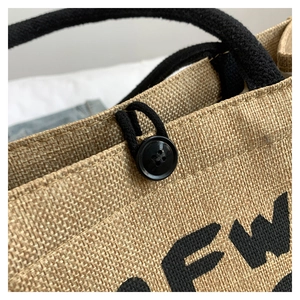 Detail of jute tote bag showing beige woven texture, black rope handle, and button closure