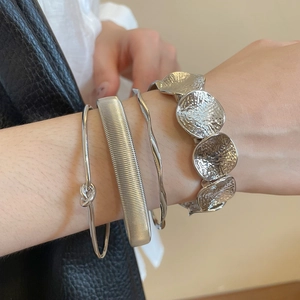 Close-up of four layered silver bracelets with brushed texture and knot designs on a wrist
