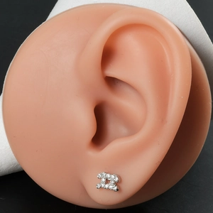 Macro shot of silver-colored double-C stud earrings with zircon crystals on an ear model