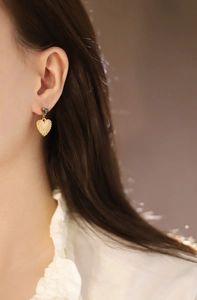 Detailed view of model wearing gold heart earrings with black round studs and textured finish
