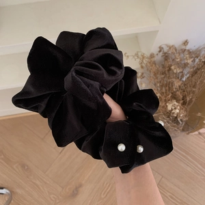 Detail of a plush black velvet scrunchie decorated with elegant white pearls held in hand