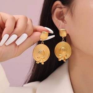 Golden straw hat pendant earrings with bow tie detail shown on model and held in hand