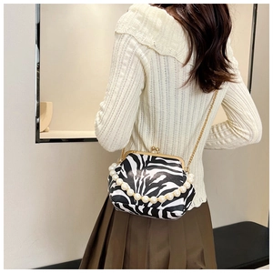 Detail of zebra pattern clutch bag featuring pearl handle and gold metal chain strap