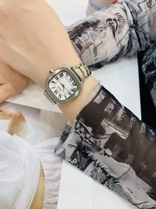 Close-up of a silver square watch with Roman numerals on a model wrist against fabric