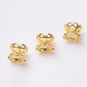 Macro detail of three 14K gold-plated hollow butterfly-shaped earring backs on white fabric