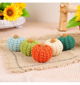 Close-up of five colorful knitted pumpkins with wooden stems on a rustic linen cloth