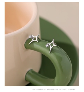 Macro shot of silver North Star stud earrings with zircon stone on green cup handle