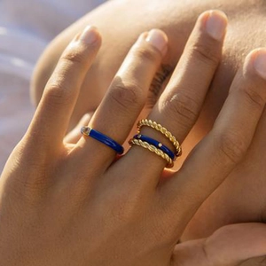Detail shot of stacked gold rings with deep blue enamel and zircon on female fingers