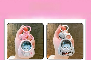 Detailed view of cartoon space capsule keychains featuring pink cat and grey monster designs