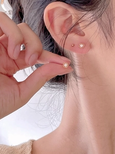 Close-up of golden flower stud earring with white pearl on a model's ear lobe