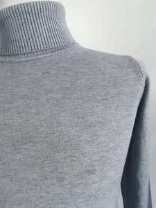 Detailed close-up of the ribbed turtleneck and shoulder seam on this gray knit sweater