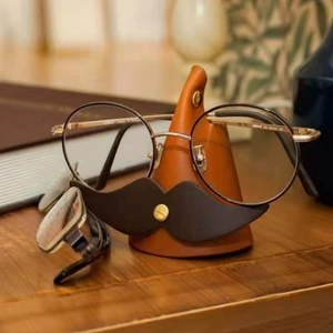 Detail of creative mustache-shaped leather glasses holder on wooden desk with metal clip