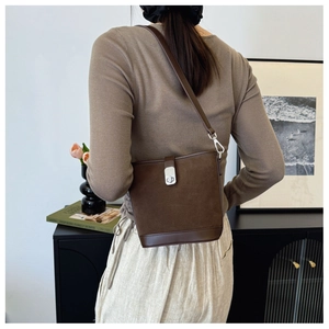 Detail of a brown matte suede bucket bag with a metal twist lock and slim shoulder strap