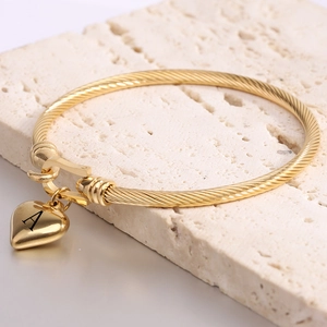Detail of twisted 18K gold-plated stainless steel bangle with heart-shaped letter A charm
