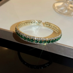 Detail view of open gold bracelet with emerald green and white cubic zirconia stones