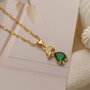 Macro view of gold boy pendant with green pear-cut zircon and crystal pavé on leafy chain