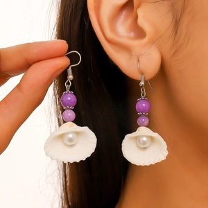 Close-up of shell earrings featuring purple beads and white pearls on a model