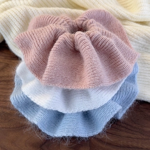 Detail of pink, white, and blue knit scrunchies showing soft wool texture on a wooden surface