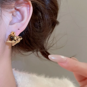Macro shot of irregular lava gold stud earring with a central dark round bead on ear