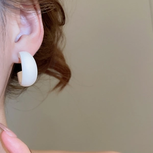 Gros plan d'une boucle d'oreille blanche en forme de C portée avec finition mate