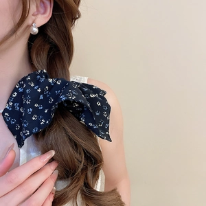 Close-up of a large navy floral bow hair tie on a model's braided brown hair