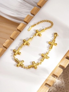 Detailed macro shot of an 18k gold plated stainless steel cross charm bracelet on wood