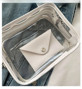 Close-up of a clear PVC crossbody bag featuring a white leather inner envelope pouch
