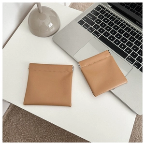 Close-up of small camel leather storage pouch with spring clasp on white desk