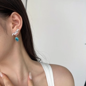 Detail of s925 silver earring featuring blue teardrop zircon on female model