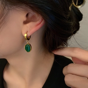 Detailed close-up of emerald green drop earrings with vintage gold finish on a model