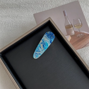 Detail of blue marble texture resin hair clip placed on a brushed metal tray