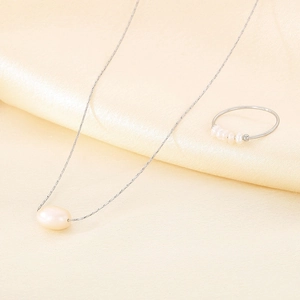 Detail of silver titanium necklace with pearl pendant and matching ring on silk fabric