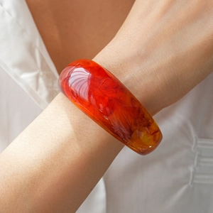Detailed close-up of a wide red resin bangle with amber texture on a woman's wrist