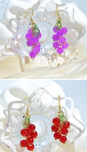 Detail of purple and red grape earrings with green leaves on white silk fabric