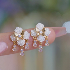 Detail of floral earrings featuring white roses, gold butterfly, and zircon tassels on fingers